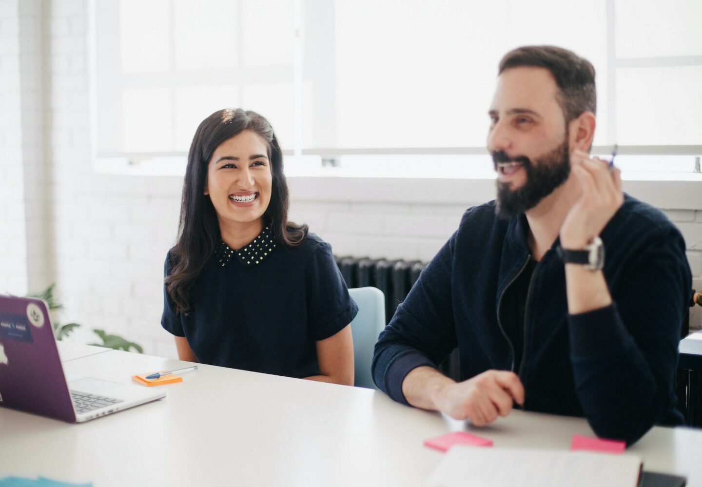 Women laughing in a meeting, with a man demonstrating a point