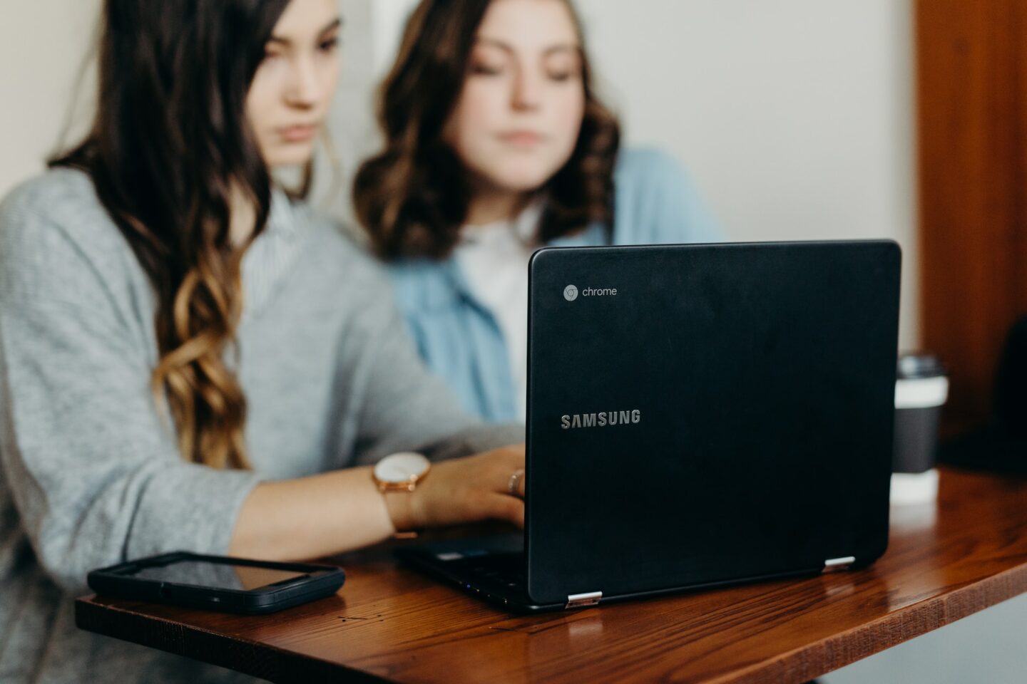 Two women working in the background on a laptop which sits in the foreground