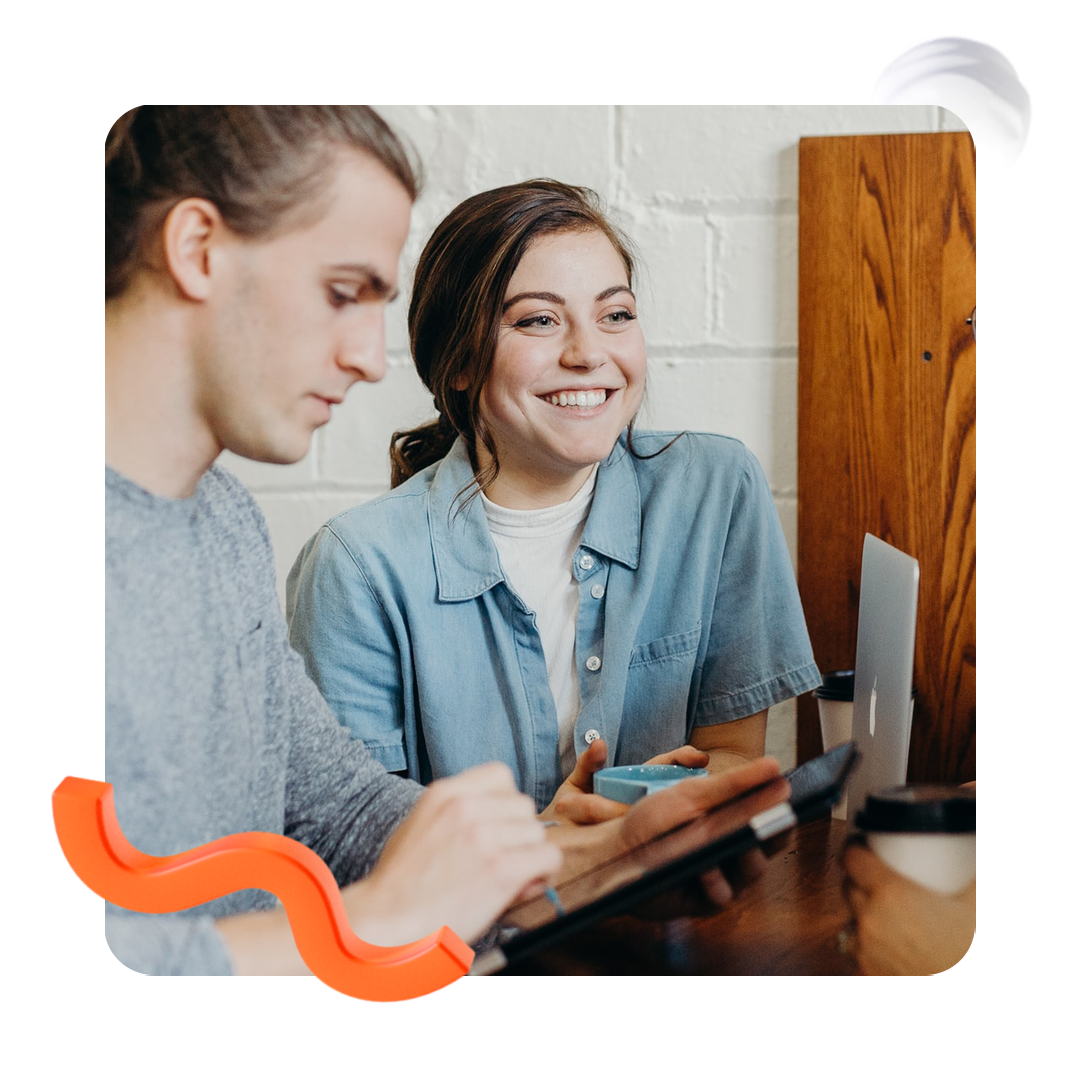 Person smiling in a cafe next to another blurred out of shot typing on a tablet